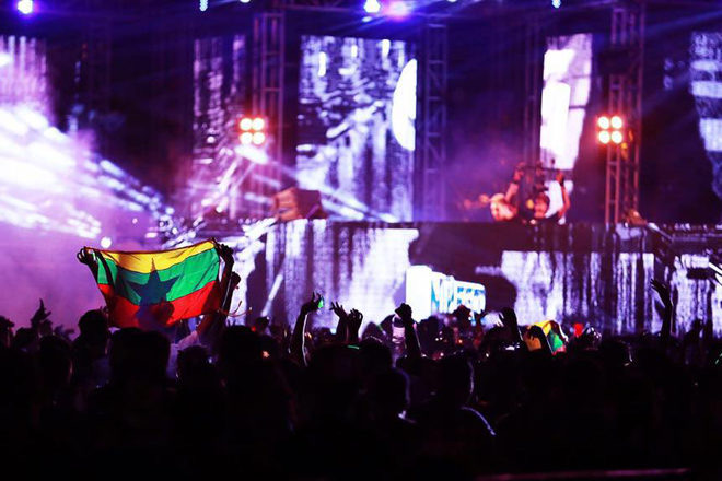 A crowd at a night-time EDM concert in Myanmar, with one person holding up the Myanmar flag in front of the stage