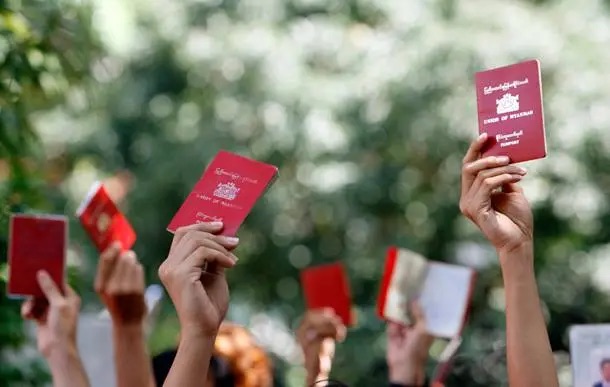 Hands raised in a crowd holding up red Myanmar passports